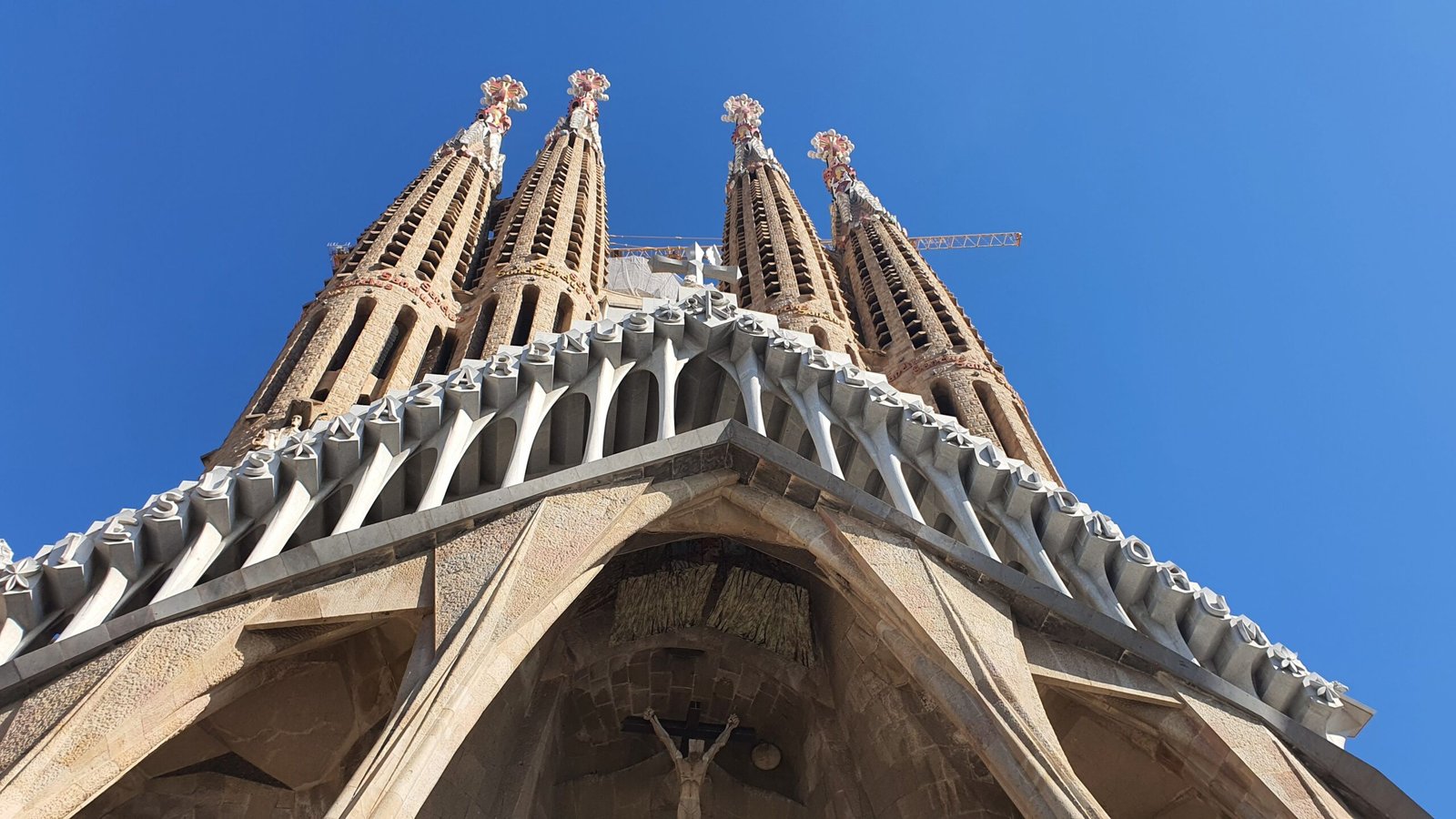 Land Tours A stunning low-angle view of Sagrada Famรญlia's intricate spires against a clear blue sky in Barcelona.